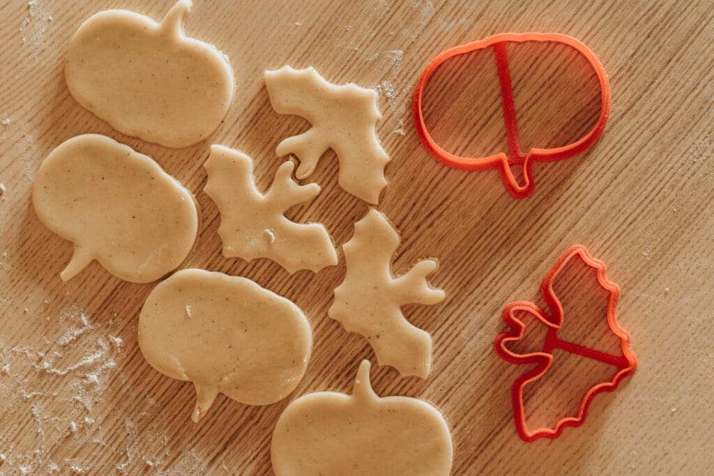 pexels-photo-5471934-5471934 Pumpkin and bat shaped cookie dough with cutters on a wooden table, perfect for Halloween baking.