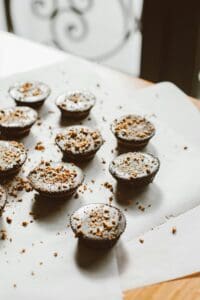 Freshly baked chocolate muffins adorned with crunchy toppings on parchment paper.